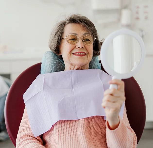 Elderly woman looking in the mirror after a failed dental implant correction procedure in Oklahoma City, OK