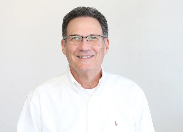 Portrait of Dr. Rusty Sullins at Warwick Dental in Oklahoma City, wearing a blue coat and smiling in the office setting.